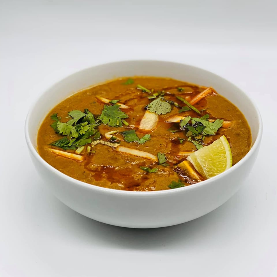 A bowl of Bangladeshi dal, garnished with fresh cilantro, ginger strips, and a lime wedge.