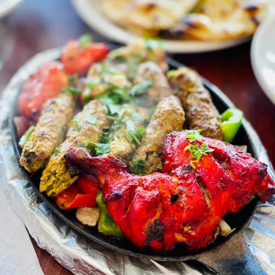 Sizzling platter of Bangladeshi tandoori chicken, seekh kebab, and vegetables, garnished with cilantro.