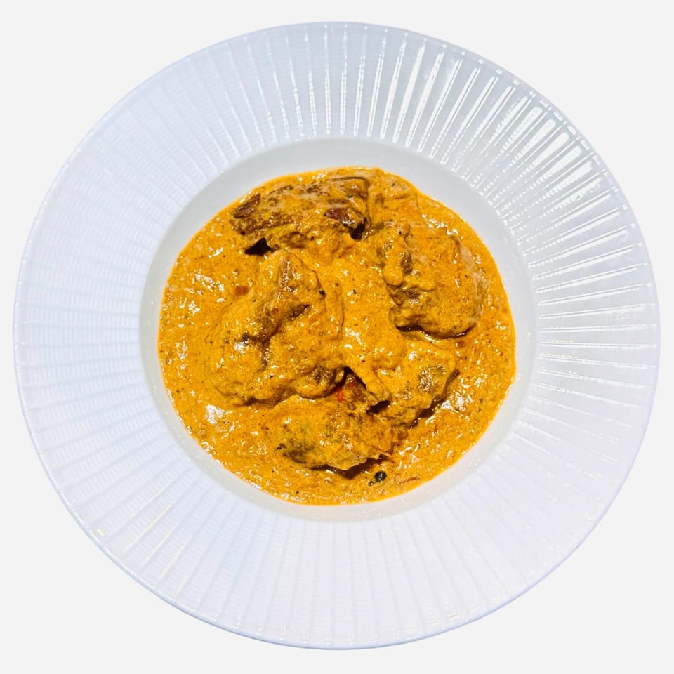 A white bowl filled with a rich, orange-colored Bangladeshi curry with chunks of meat.