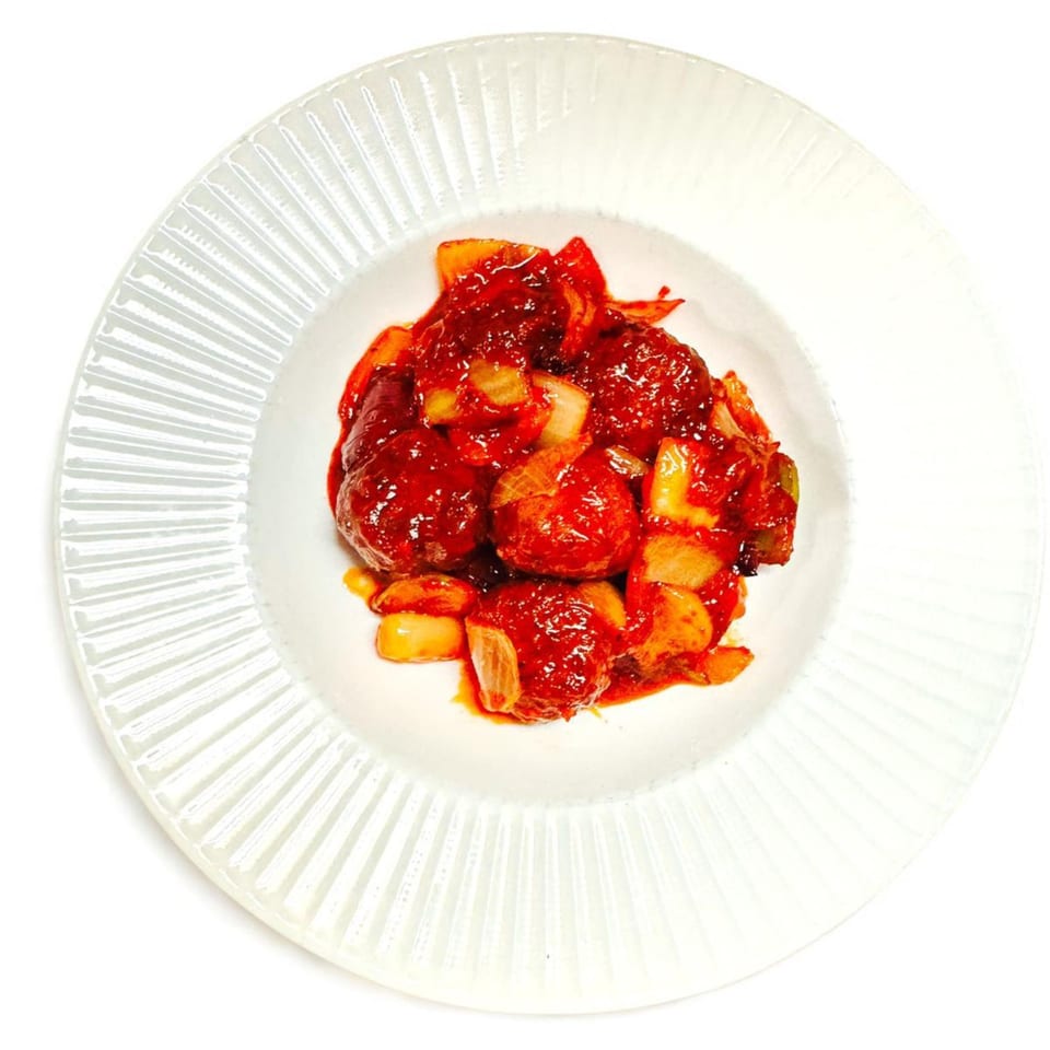 Chameli Restaurant's Bangladeshi meatballs in a rich red sauce with onions, served on a white plate.