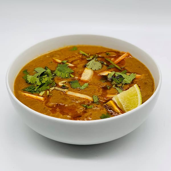 A bowl of Chameli Restaurant's Bangladeshi haleem, garnished with cilantro, ginger, and a lime wedge.