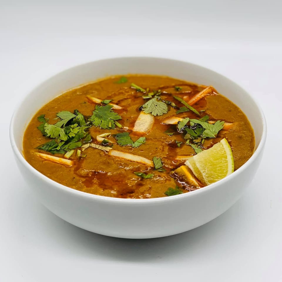 A bowl of Chameli Restaurant's Bangladeshi haleem, garnished with cilantro, ginger, and a lime wedge.