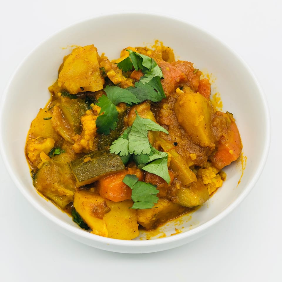 A white bowl filled with a vibrant Bangladeshi vegetable curry, garnished with fresh cilantro.