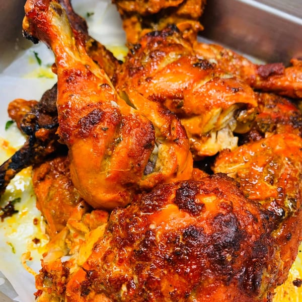 Close-up of several pieces of golden-brown roasted chicken with crispy skin, likely Chameli Restaurant's Bangladeshi cuisine.