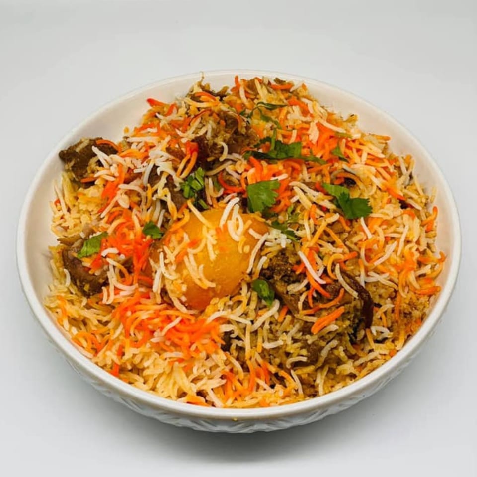 A white bowl filled with Bangladeshi biryani, featuring rice, meat, potatoes, and cilantro.