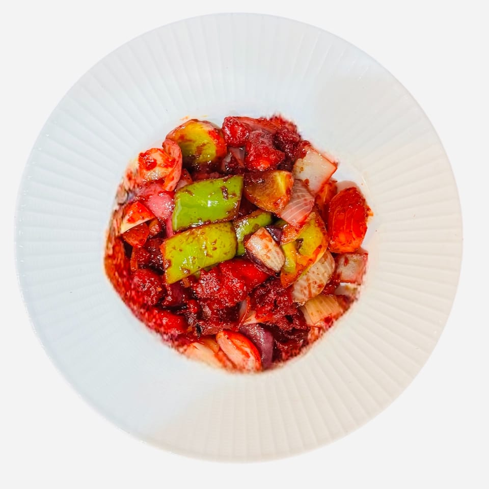 A vibrant Bangladeshi dish with red sauce, green peppers, and onions on a white plate.