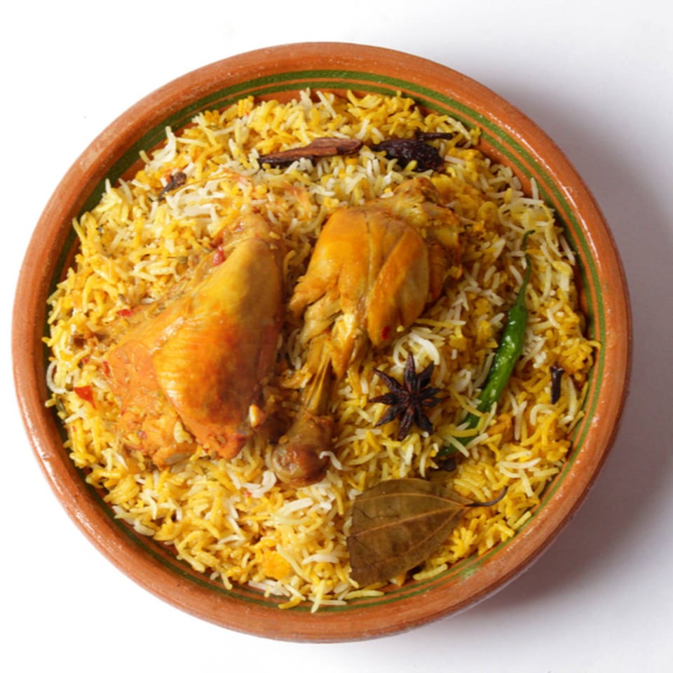 Chicken biryani with two chicken pieces, rice, and spices in a brown bowl.