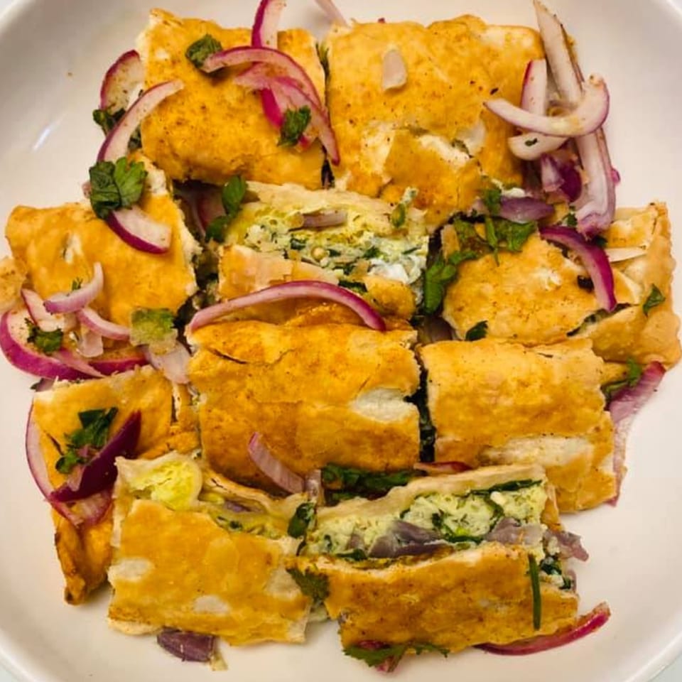 Golden Bangladeshi omelet pieces with green herbs and red onion slices on a white plate.