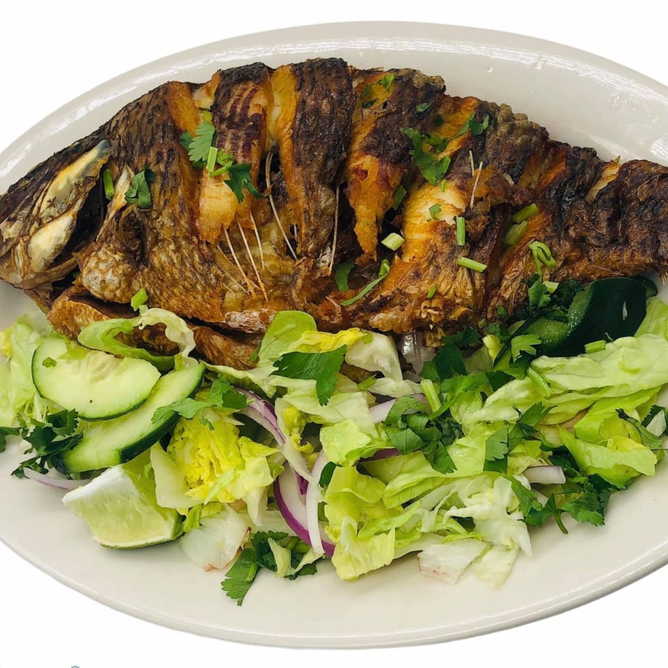 Whole fried fish garnished with cilantro and green onions, served with a fresh salad.