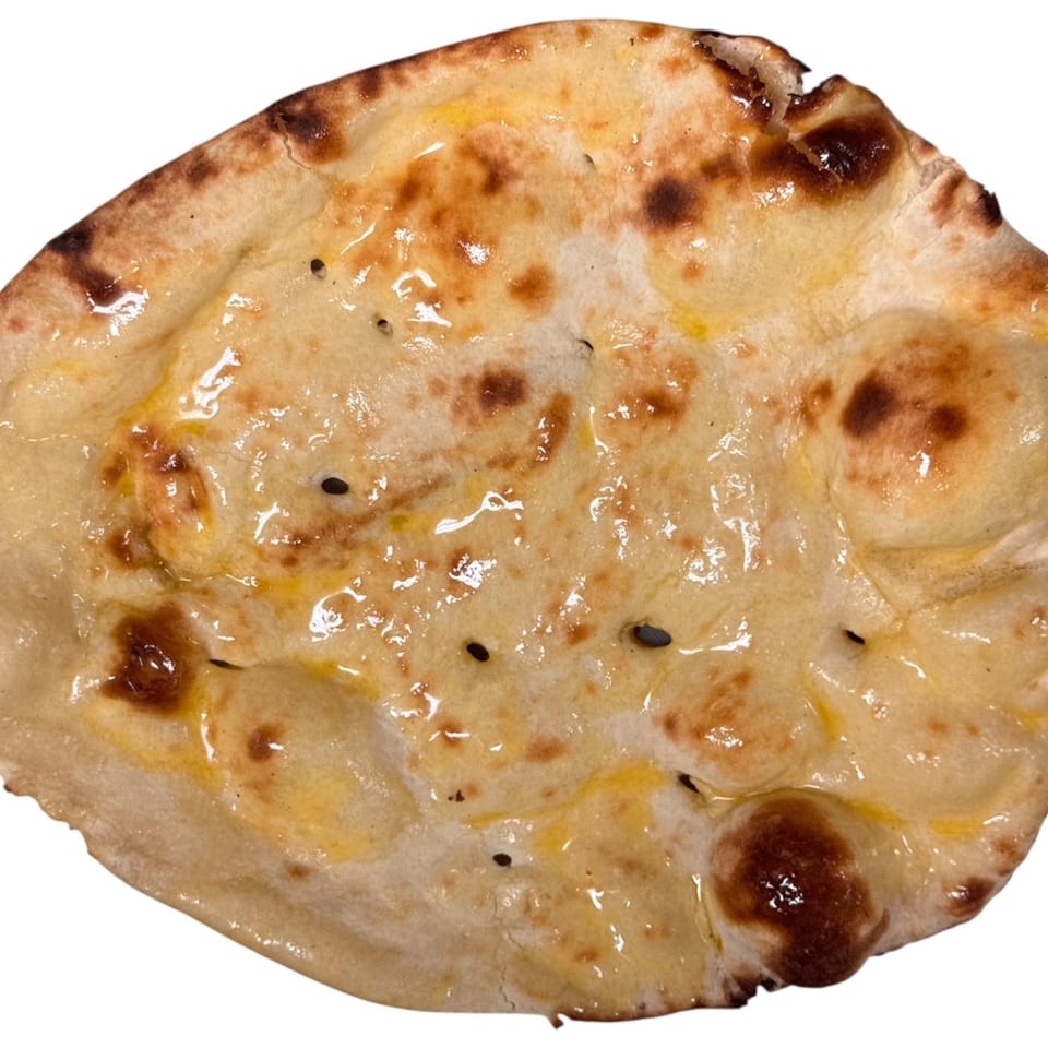 Close-up of a golden-brown Bangladeshi naan bread, glistening with butter and sprinkled with black seeds.