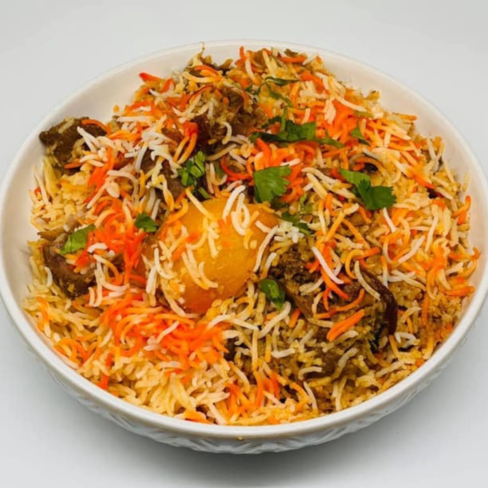 A white bowl filled with colorful Bangladeshi biryani, featuring rice, meat, and a potato, garnished with cilantro.