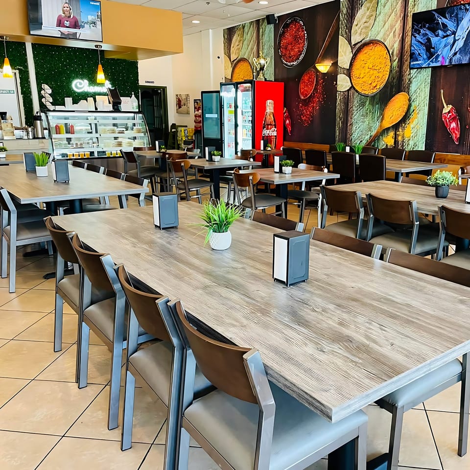 Interior of Chameli Restaurant with dining tables, chairs, a food display case, and spice-themed wall art.