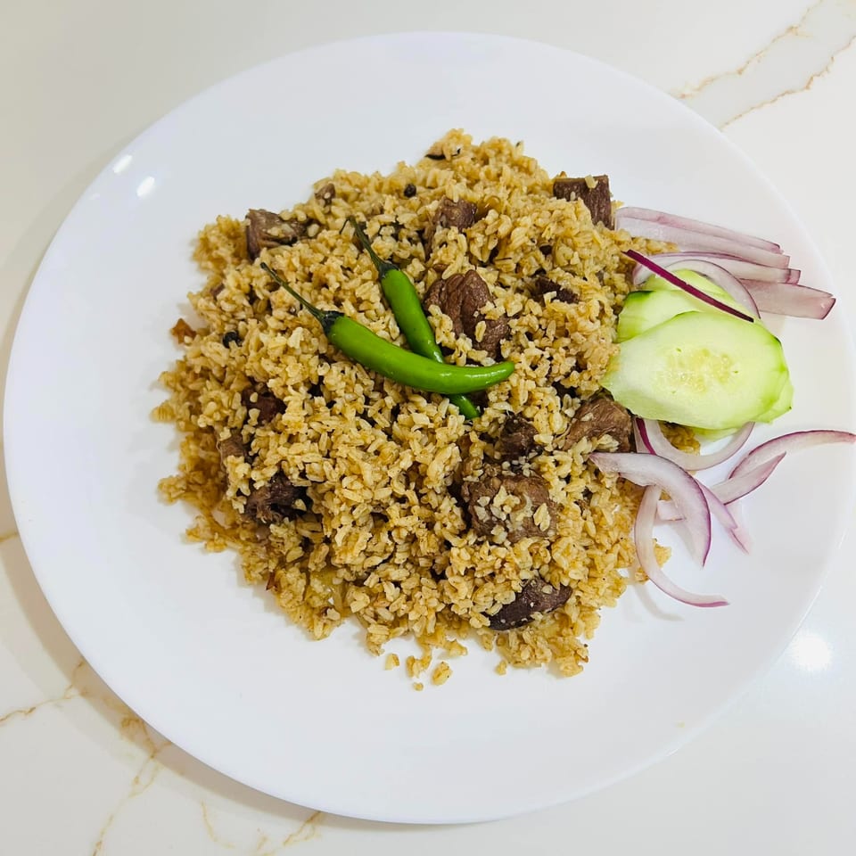 A plate of Bangladeshi beef khichuri with green chilies, sliced red onions, and cucumber.