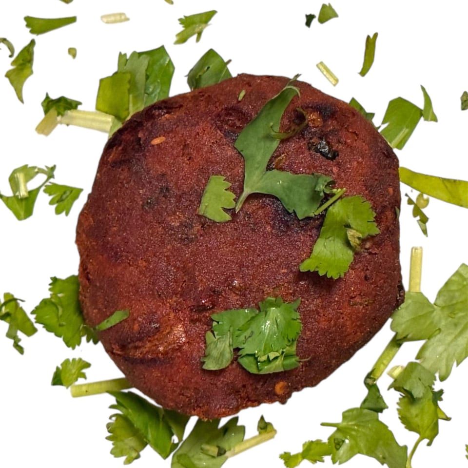 A round, reddish-brown Bangladeshi Chameli Restaurant cutlet, garnished with fresh green cilantro on a white background.