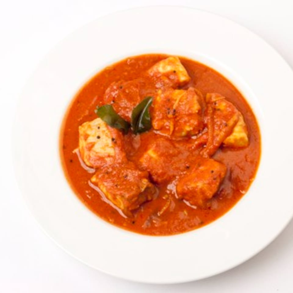 A white bowl filled with Chameli Restaurant's Bangladeshi fish curry in a rich red sauce.