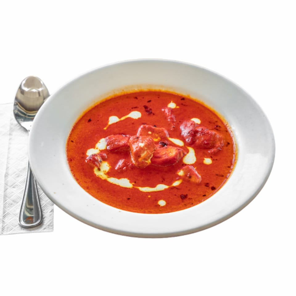 A white bowl of Chameli Restaurant's vibrant red Bangladeshi curry with chicken and cream swirls.