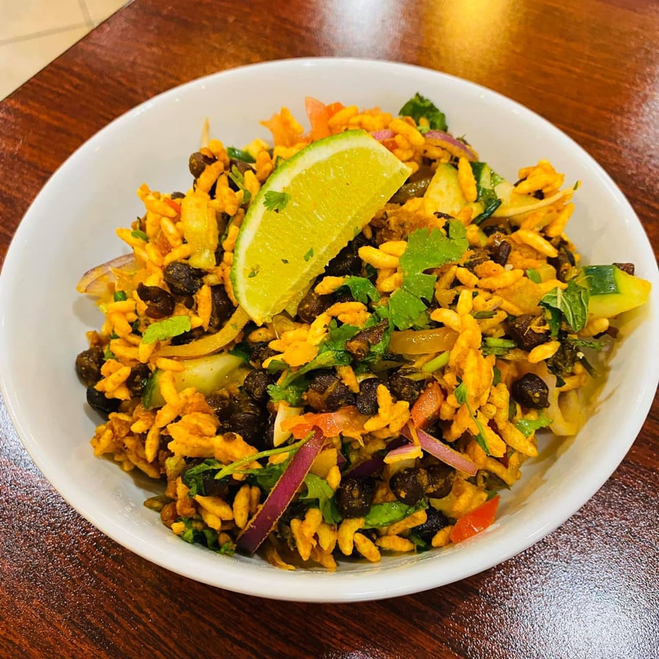 A white bowl of Bangladeshi Jhal Muri with puffed rice, black chickpeas, and a lime wedge.