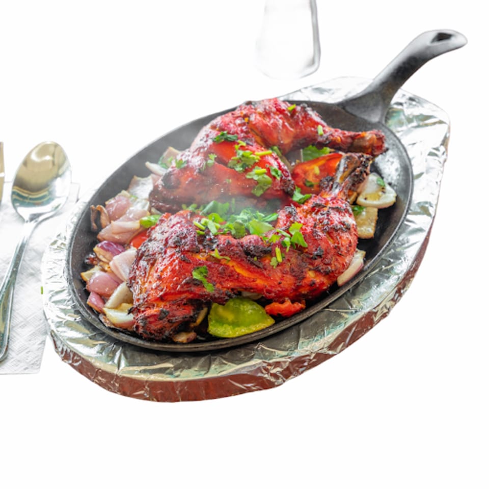Sizzling Bangladeshi tandoori chicken with onions and peppers in a hot skillet, garnished with cilantro.