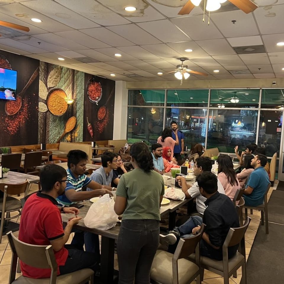 Diners enjoying a meal at Chameli Restaurant, with a spice-themed mural and large windows.