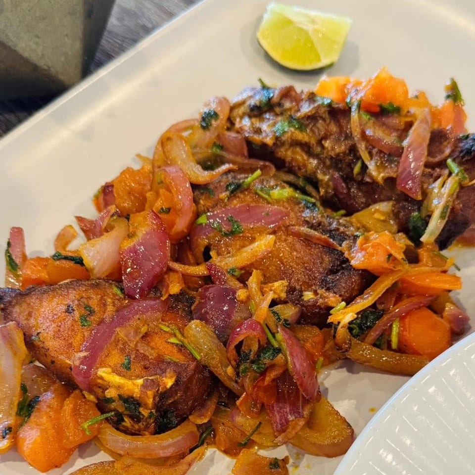 Chameli Restaurant's Bangladeshi fish curry with red onions, carrots, and a lime wedge.