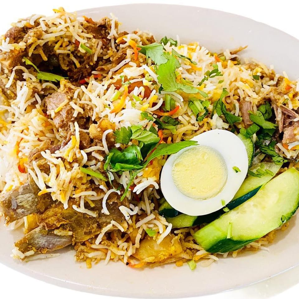 A plate of Chameli Restaurant's Bangladeshi biryani with meat, rice, cilantro, a hard-boiled egg, and cucumber slices.