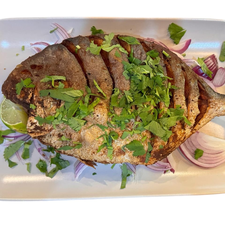 Whole fried fish garnished with fresh cilantro, red onion slices, and a lime wedge on a white plate.